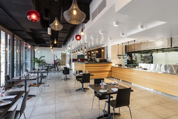 Un restaurant moderne doté de nombreuses tables et chaises, d’un bar et de grandes fenêtres laissant entrer la lumière naturelle.