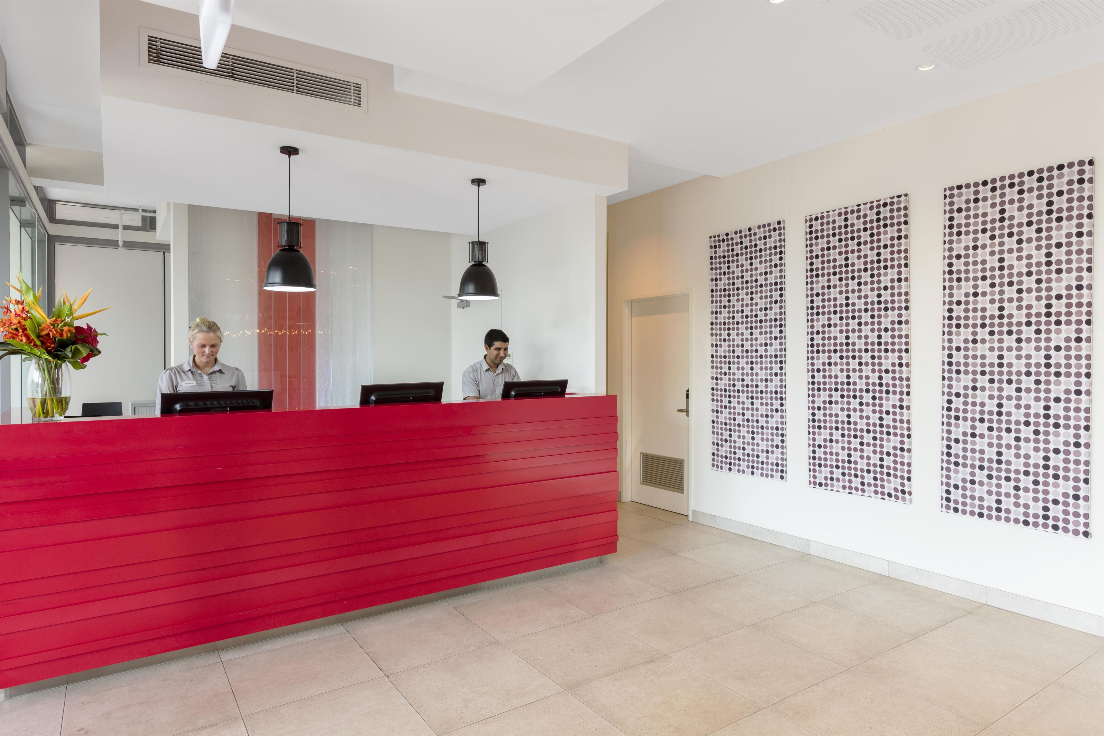 A reception desk with two staff members, a red counter, black pendant lights, and a wall with a polka dot pattern.