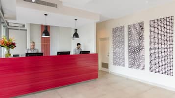 A reception desk with two staff members, a red counter, black pendant lights, and a wall with a polka dot pattern.
