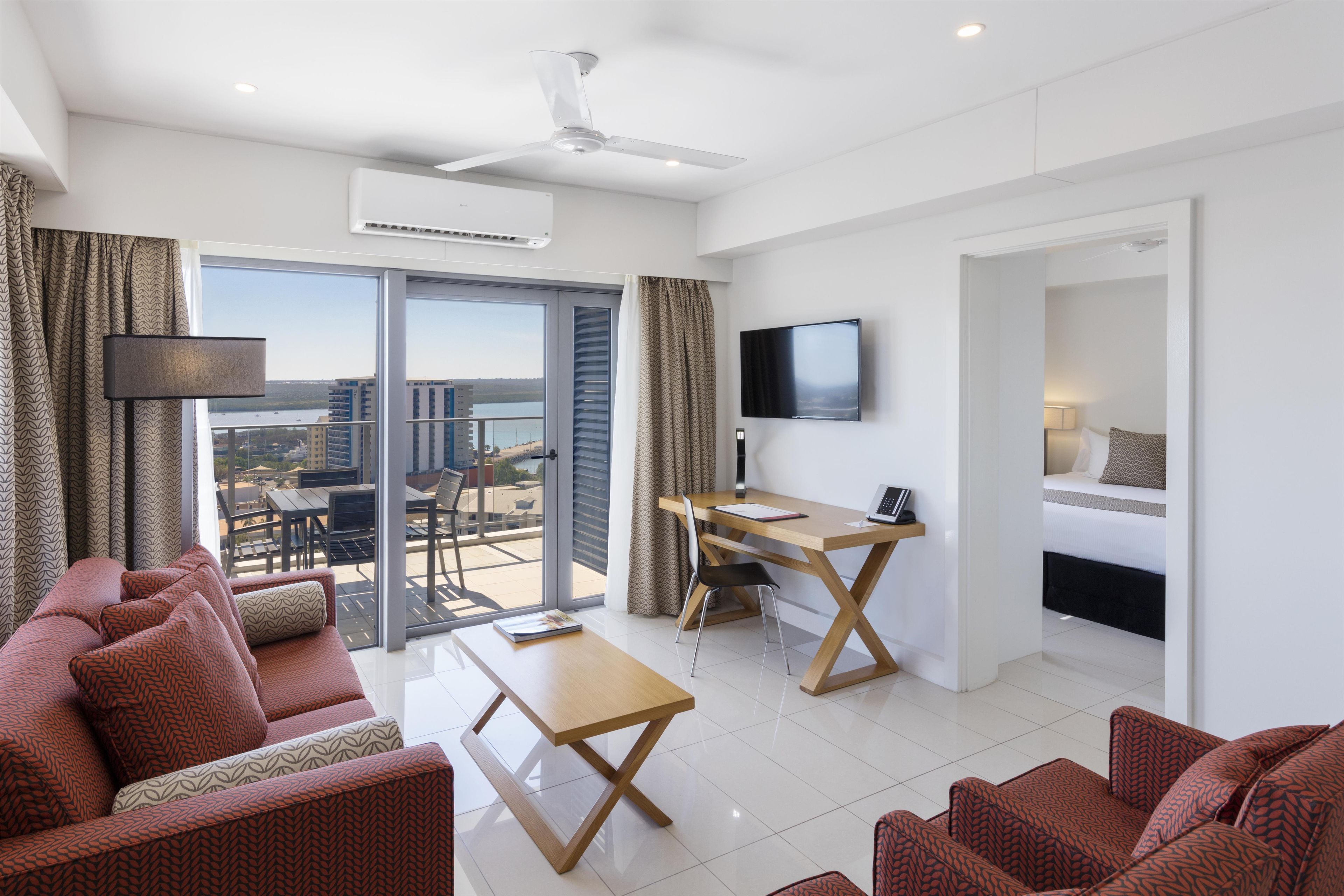 Et moderne hotelværelse med balkon, fladskærms-tv, skrivebord og sofa.