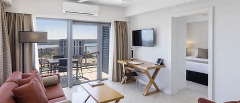 Et moderne hotelværelse med balkon, fladskærms-tv, skrivebord og sofa.