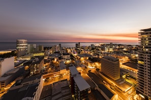 Une vue aérienne d’une ville au crépuscule, avec ses bâtiments, ses rues et un coucher de soleil sur l’eau.