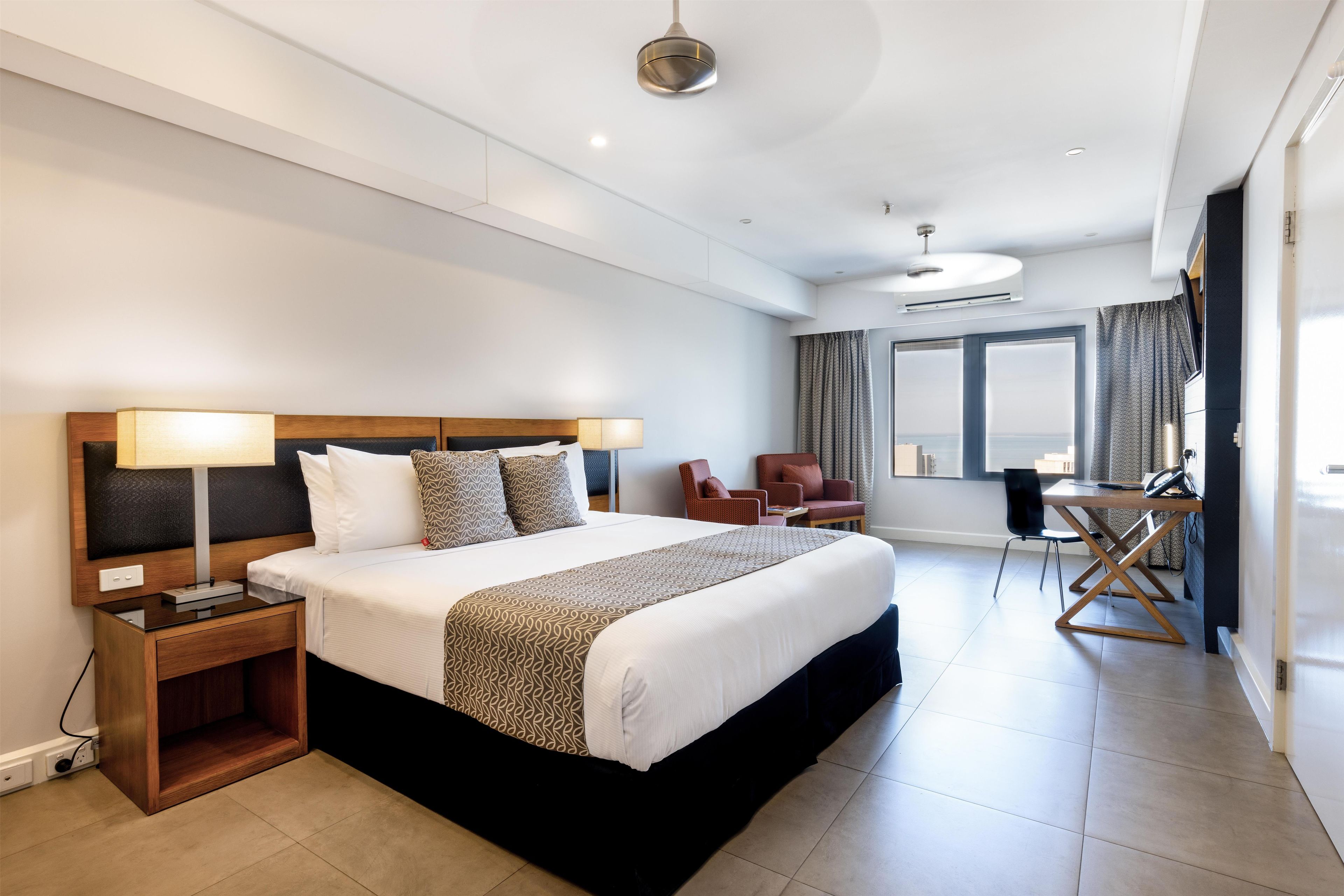 A modern hotel room with a large bed, bedside lamps, a desk, and a view of the sea.