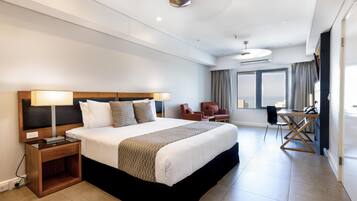 A modern hotel room with a large bed, bedside lamps, a desk, and a view of the sea.