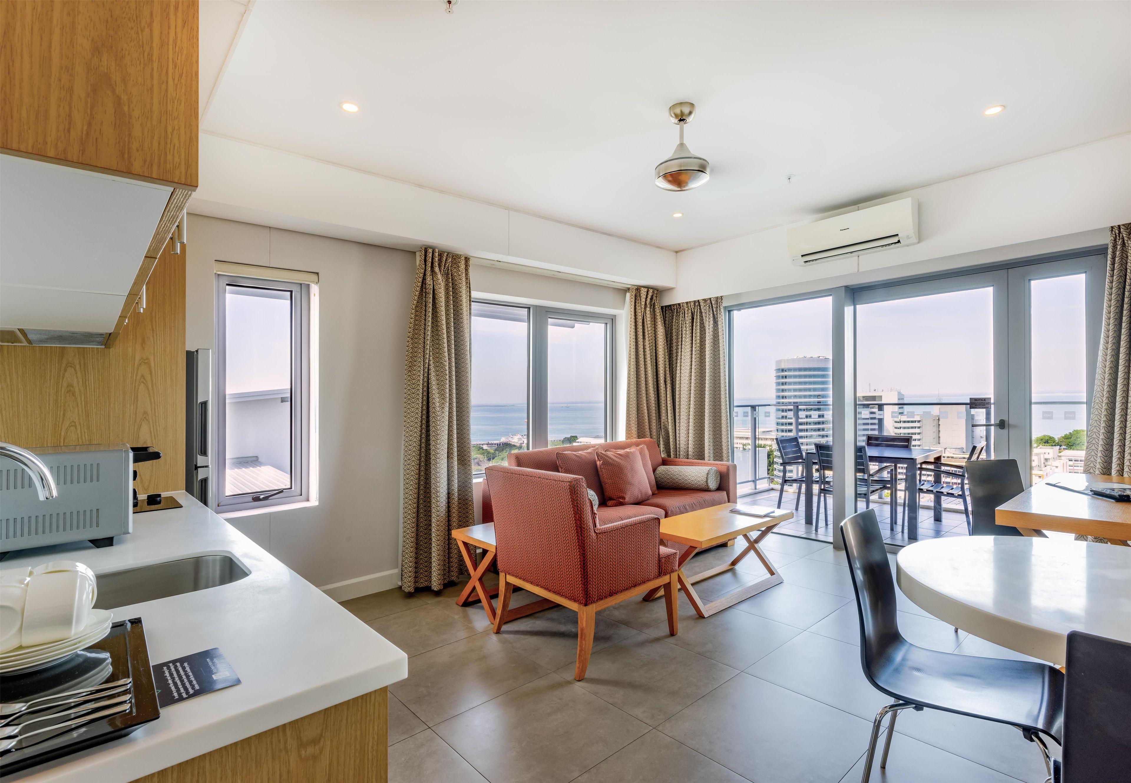 Et moderne hotelværelse med balkon, sofaarrangement, spisebord og tekøkken.