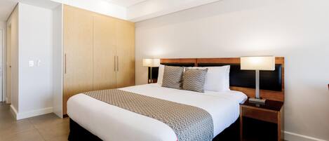 A modern hotel room with a large bed, bedside lamps, a wardrobe, and a door leading to another room.