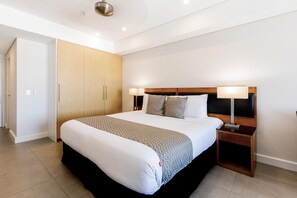 Une chambre d’hôtel moderne avec un grand lit, des lampes de chevet, une armoire et une porte donnant sur une autre pièce.