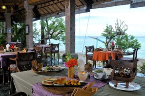 Un área de comedor al aire libre con mesas dispuestas para comidas, con vista a la playa.