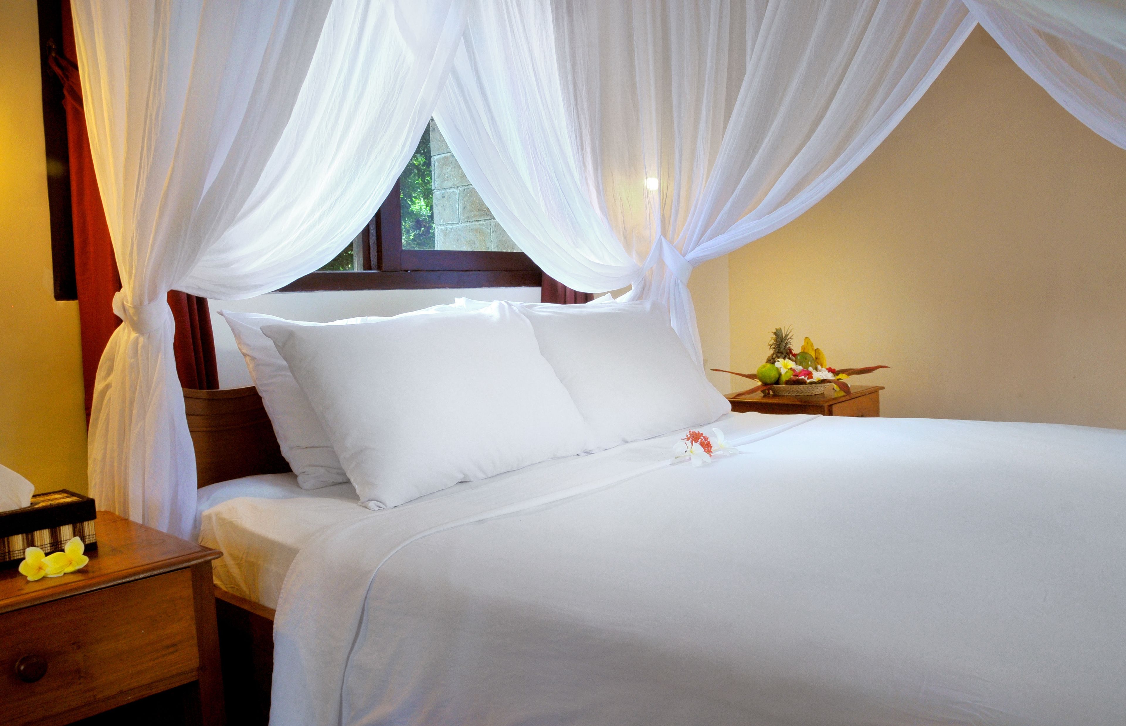 A neatly made bed with white linens and a canopy.