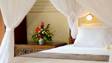 Una cama con sábanas blancas, una mesita de noche con un florero y una lámpara de pared.