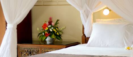 A bed with white linens, a bedside table with a vase of flowers, and a wall-mounted lamp.