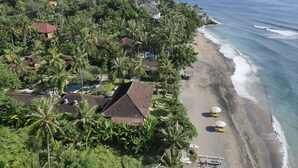 An aerial view of a coastal resort with a beach, palm trees, and a swimming pool. - Hidden Paradise Cottages (Karangasem)