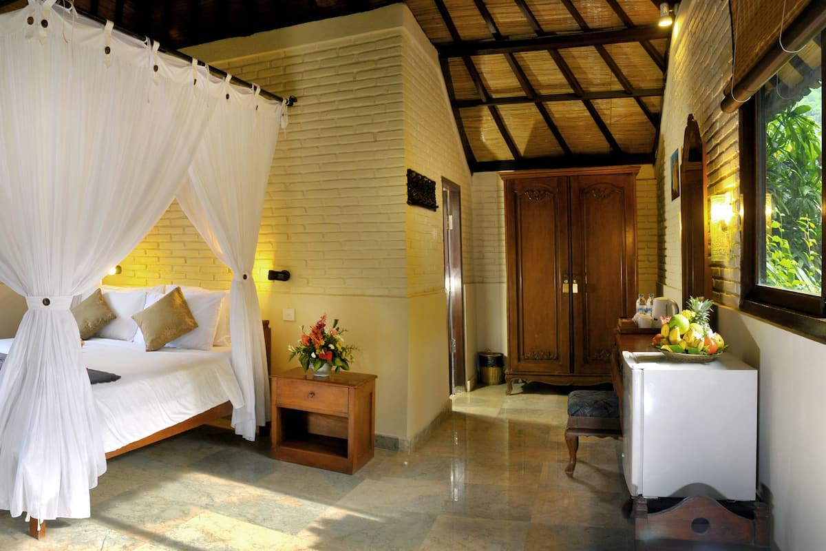 A bedroom with a four-poster bed, a wooden nightstand, a small table with a fruit bowl, and a wardrobe.