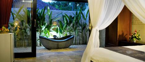 Un dormitorio con cama, ventana grande y vista a un jardín.