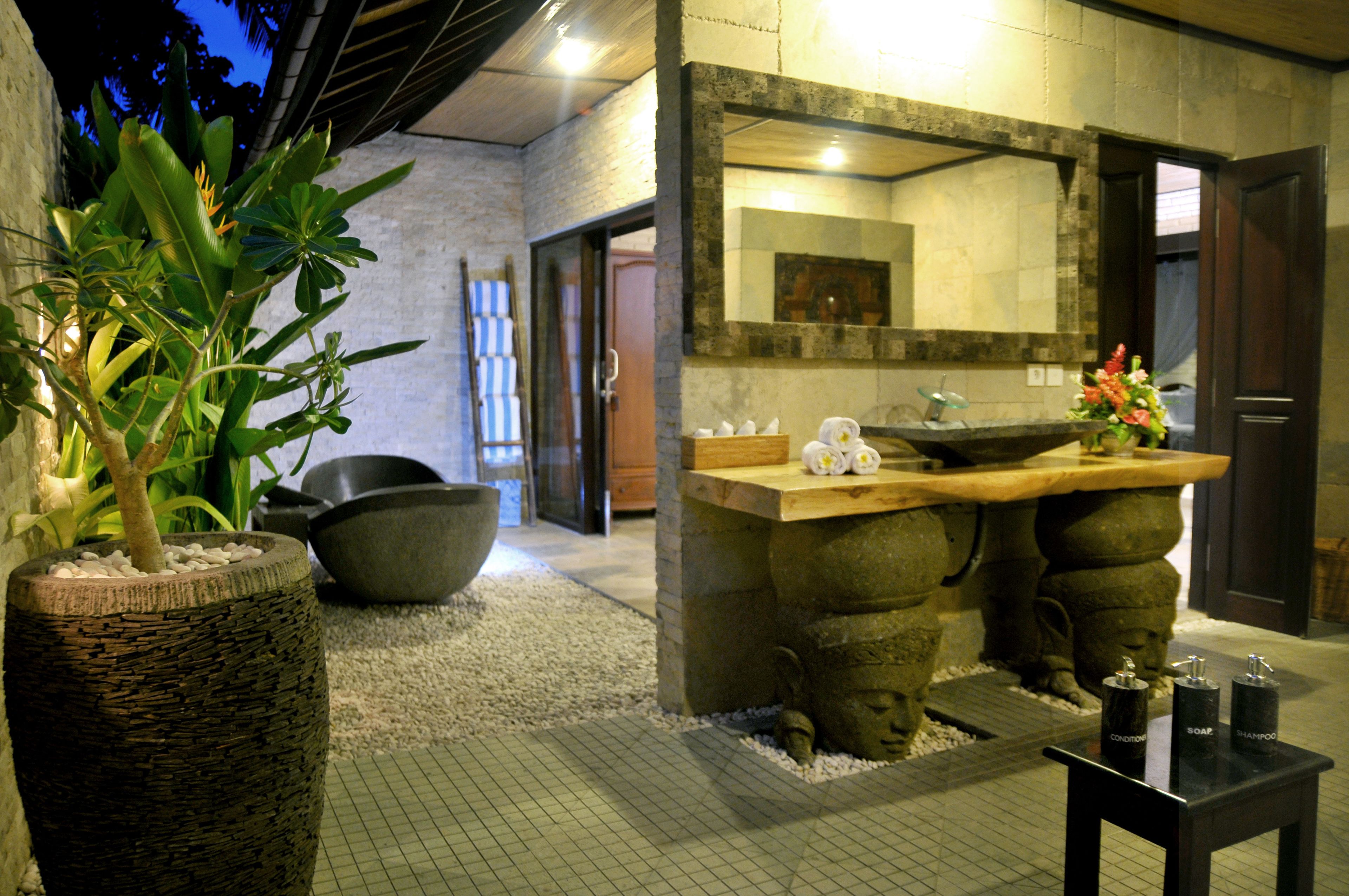 A modern bathroom with a stone sink, a large mirror, and a potted plant.