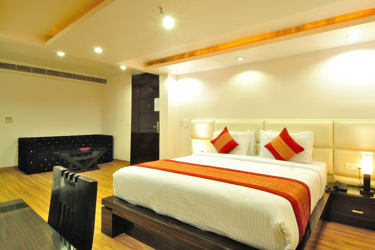 Habitación de hotel con una cama grande, lámparas de noche, una mesita de noche y un banco de madera.