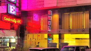 Un hotel con un letrero de neón que dice "ELEGANCE" y un cartel visible de "Center City A/C".
