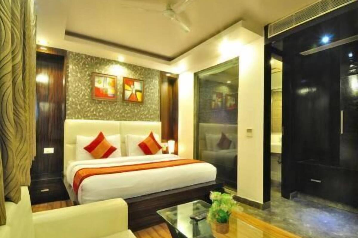 Una habitación de hotel con cama, sofá, una mesa de centro de vidrio y una pared decorada con obras de arte.