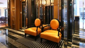 A lobby with a modern design, featuring a reception desk, a seating area with two chairs, and a glass elevator. - APA Hotel Shimbashi Toranomon (Tokyo)