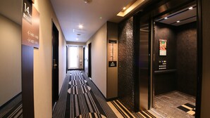 A hotel corridor with directional signs, an elevator, and a patterned carpet. - APA Hotel Shimbashi Toranomon (Tokyo)