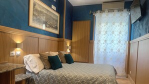 A bedroom with a bed, bedside tables, a wall-mounted light, a large framed picture, and a window with a floral curtain. - B&B A Casa di Barbara (Rome)