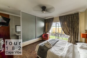 A hotel room with a bed, a TV, a red chair, and a view of the outdoors. - Cape Vibe182 (Cape Town)