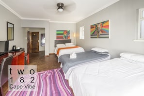 A hotel room with two beds, a desk, and artwork on the walls.