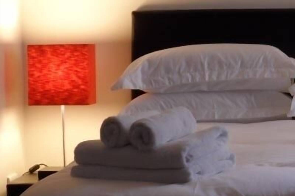 Un lit bien fait, avec du linge de lit blanc et des oreillers, un tableau abstrait rouge accroché au mur et une photo encadrée au-dessus du lit.