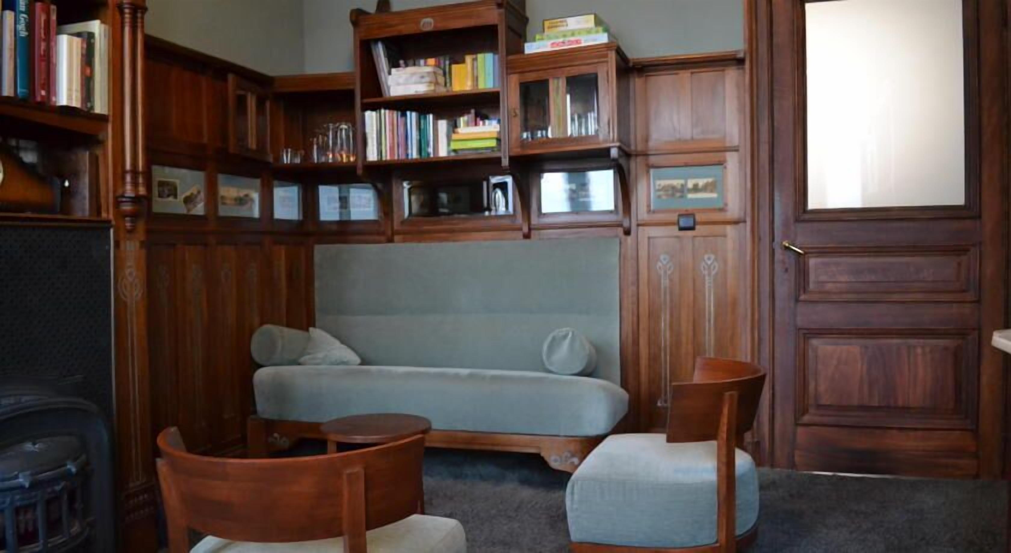 Een gezellige kamer met een bank, twee houten stoelen, een klein tafeltje en een boekenkast vol boeken.