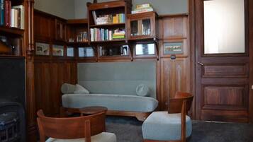 Een gezellige kamer met een bank, twee houten stoelen, een klein tafeltje en een boekenkast vol boeken.
