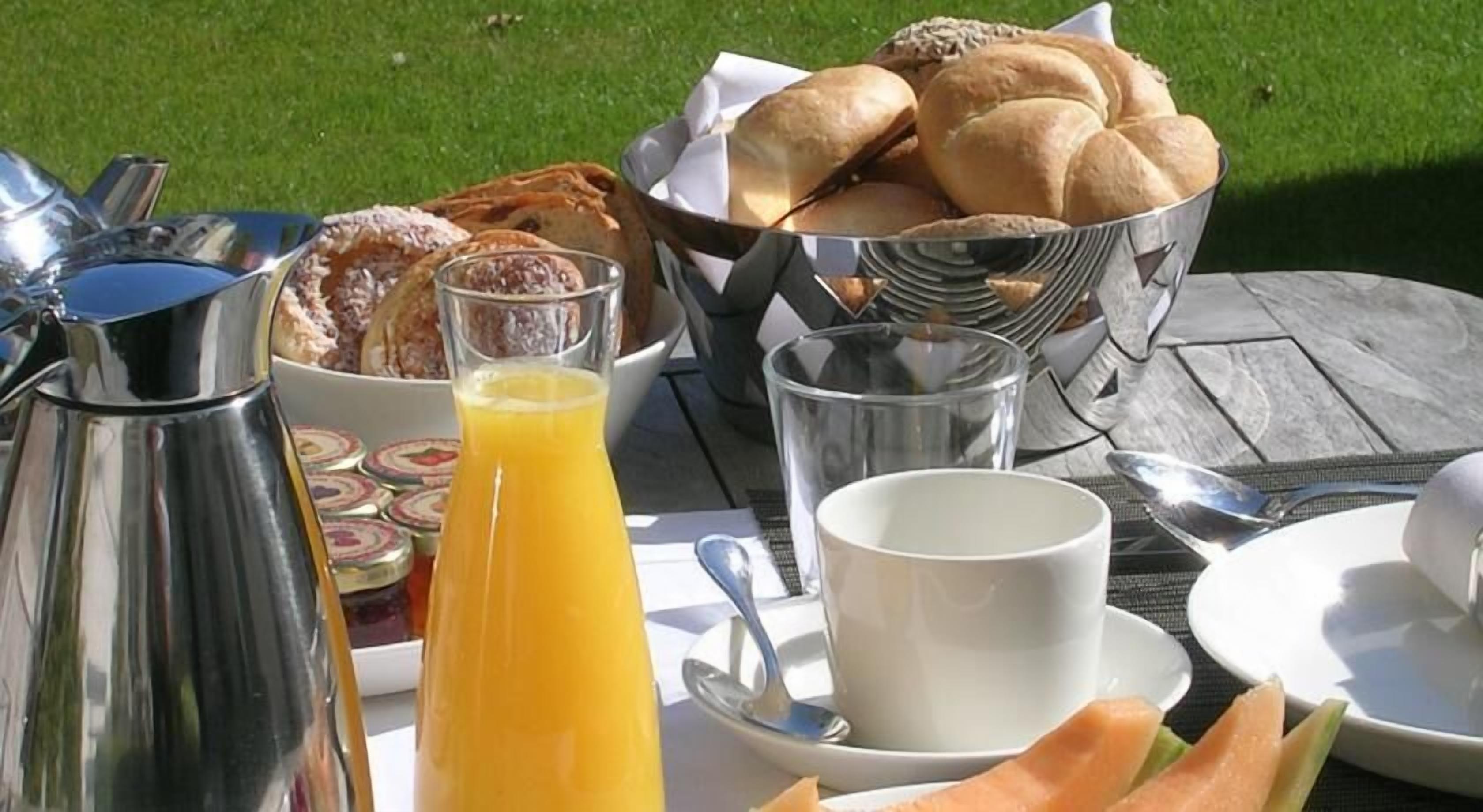 Een ontbijttafel met een koffiepot, sap, brood en gebak.