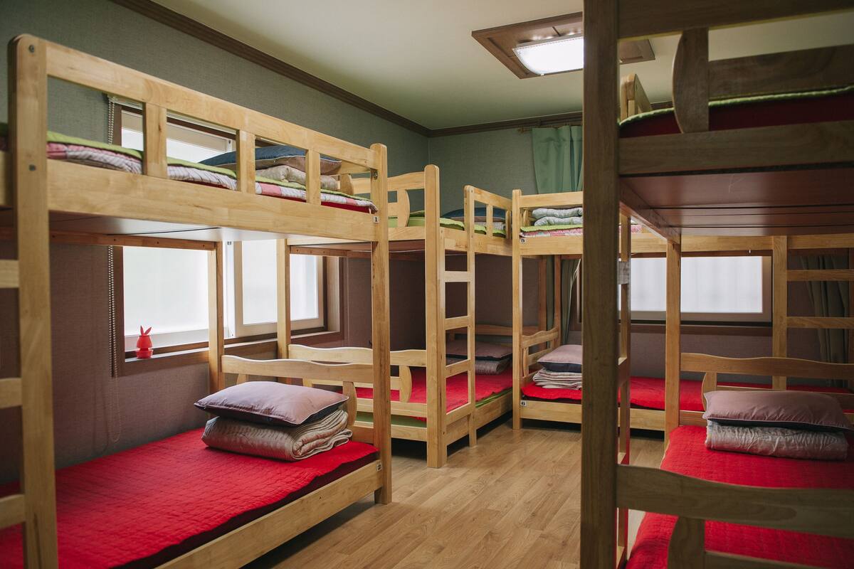 A dormitory room with bunk beds, wooden frames, and red bedding.