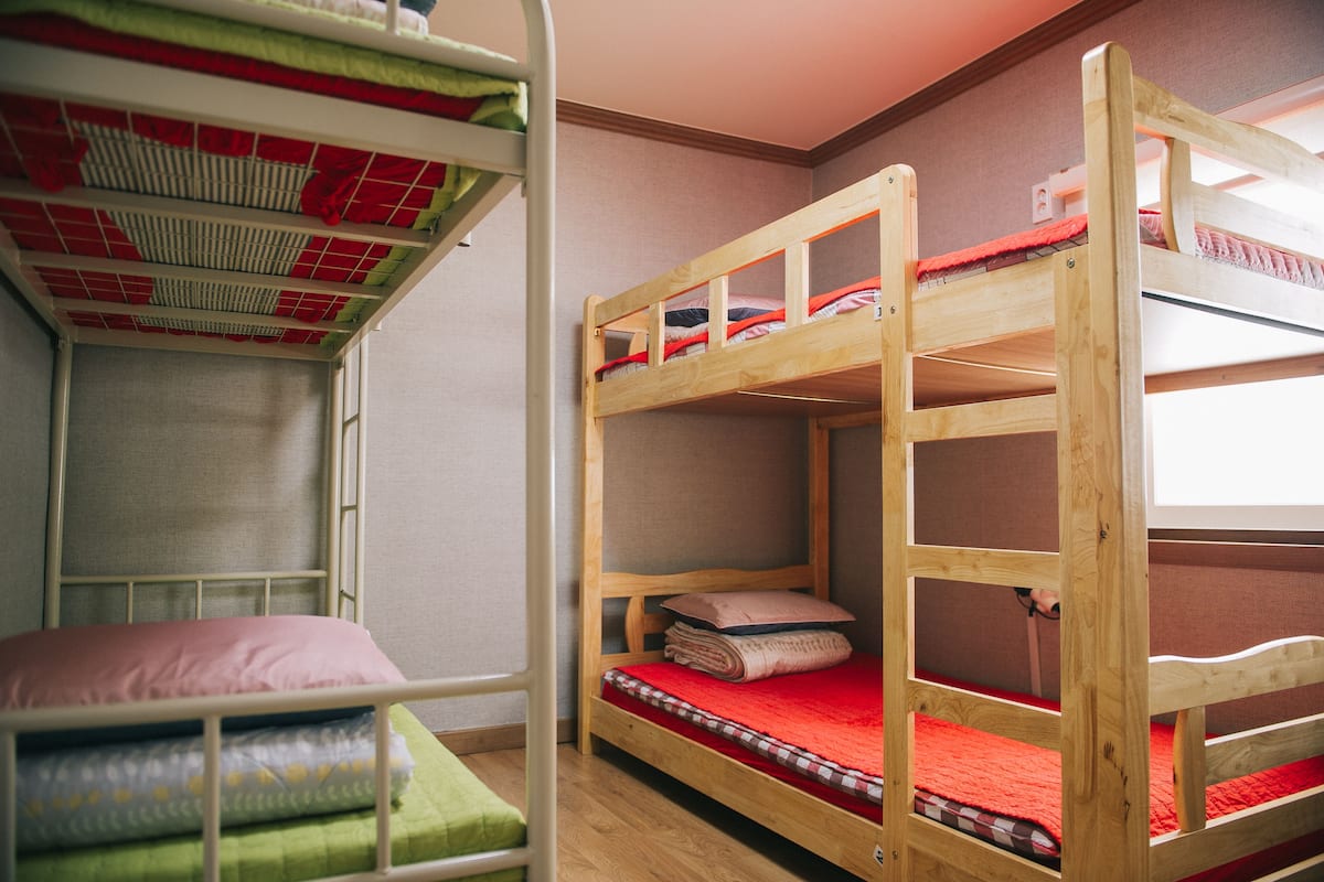 A bunk bed room with a window, wooden bunk beds, and a green bed at the bottom.