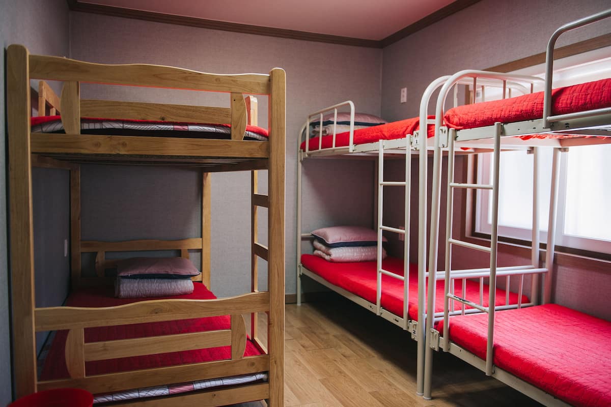 A bunk bed room with wooden and metal bunk beds, red bedding, and a wooden chair.