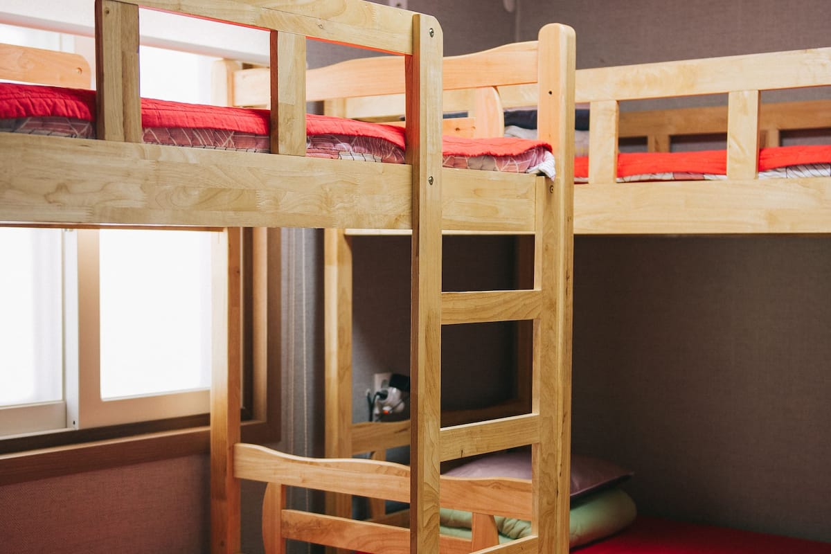 A bunk bed room with a ladder, wooden frame, and red bedding.