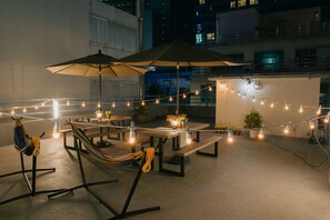 An outdoor patio area with string lights, a hammock, picnic tables, and umbrellas. - We Guest House - Hostel (Busan)