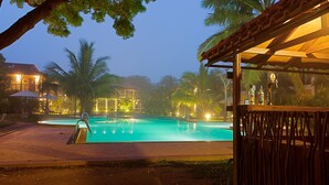 A swimming pool with a wooden deck and palm trees, surrounded by buildings with warm lighting. - Ranna 212 (Kahandamodara)