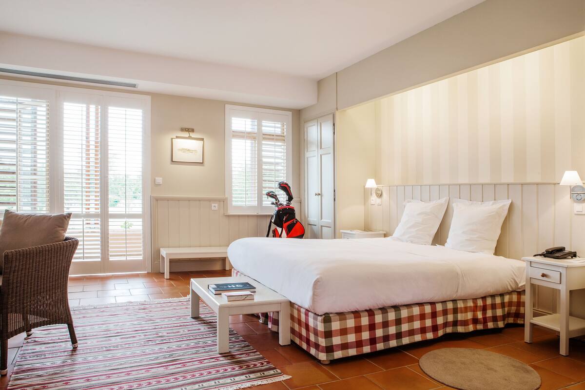 A bedroom with a large bed, a chair, a table, and a guitar.