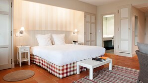 A hotel room with a large bed, bedside tables, a small table, a chair, a bathroom visible through an open door, and a patterned rug. - Relais des Vigiers (Monestier)