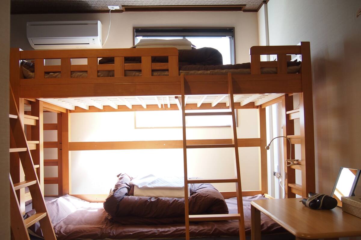 A bunk bed room with a ladder, a small table, and a window.