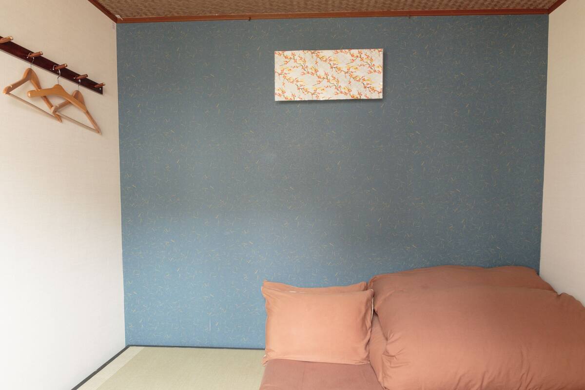 A bedroom with a blue wall, a wooden coat rack, and a framed picture.