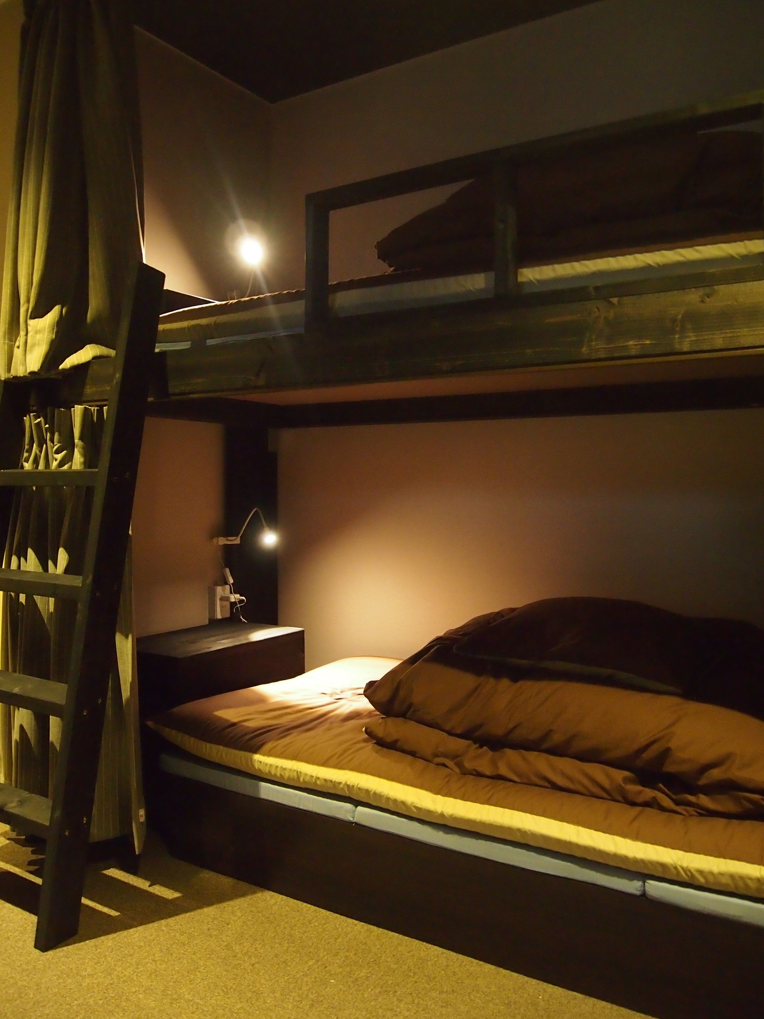 A bunk bed with a ladder, a bedside table with a lamp, and a curtain.