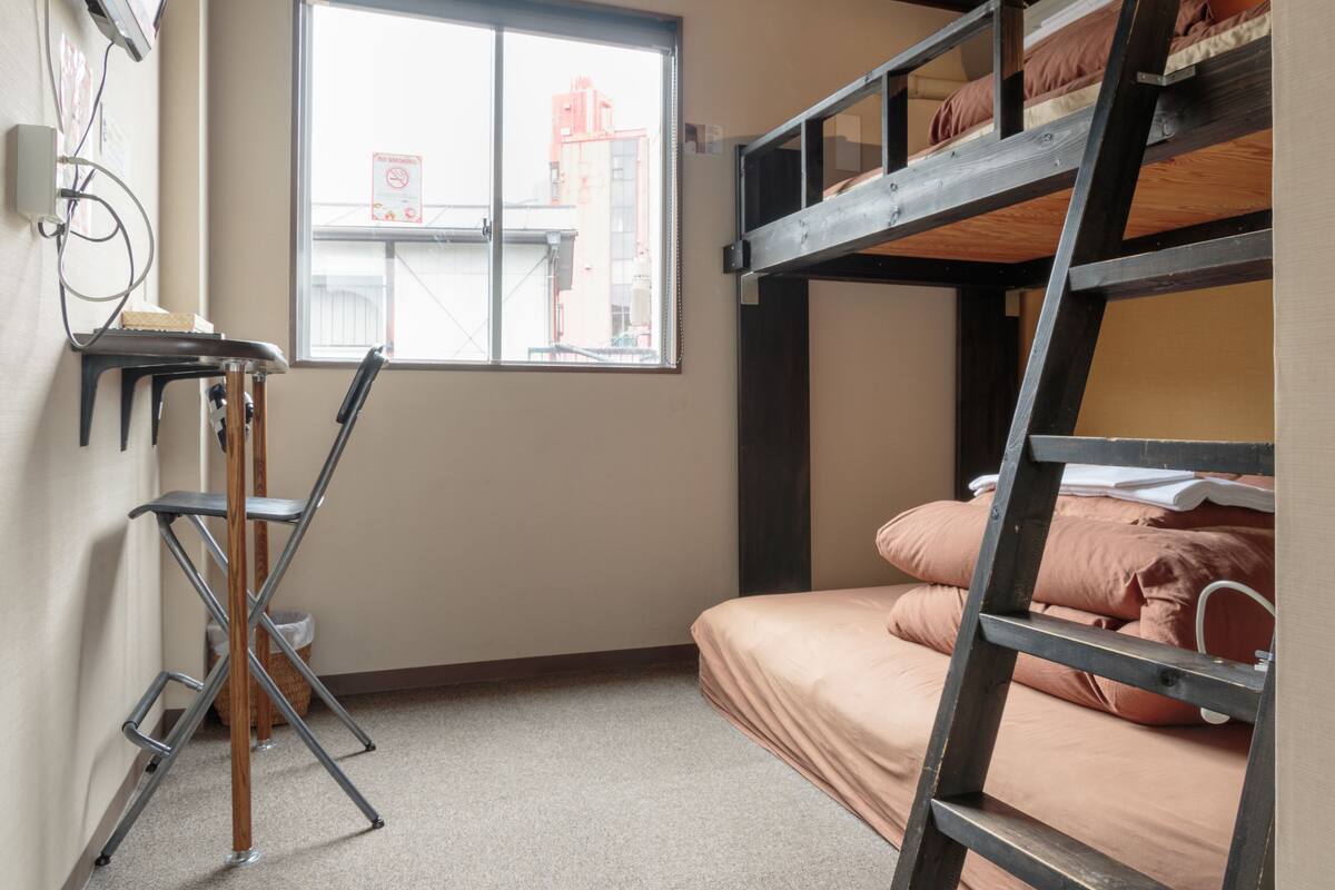 A bunk bed room with a desk and chair, a window with a view of buildings, and a no smoking sign on the wall.