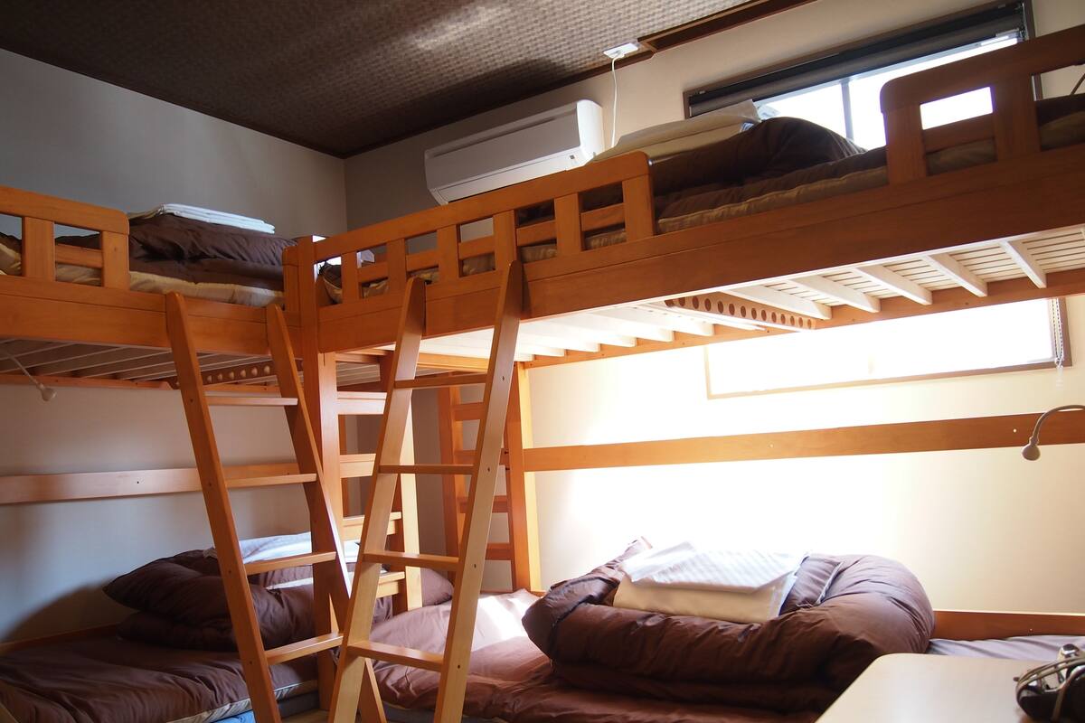 A bunk bed room with a ladder, pillows, and a table.