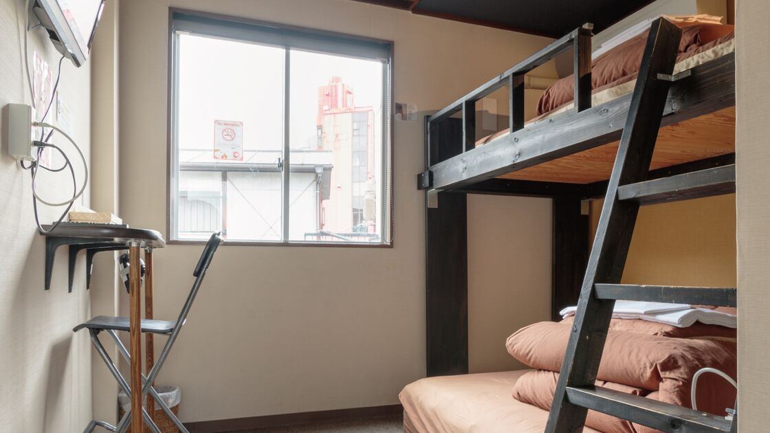 Ein Schlafraum mit Etagenbett, Fenster, Schreibtisch und Stuhl.