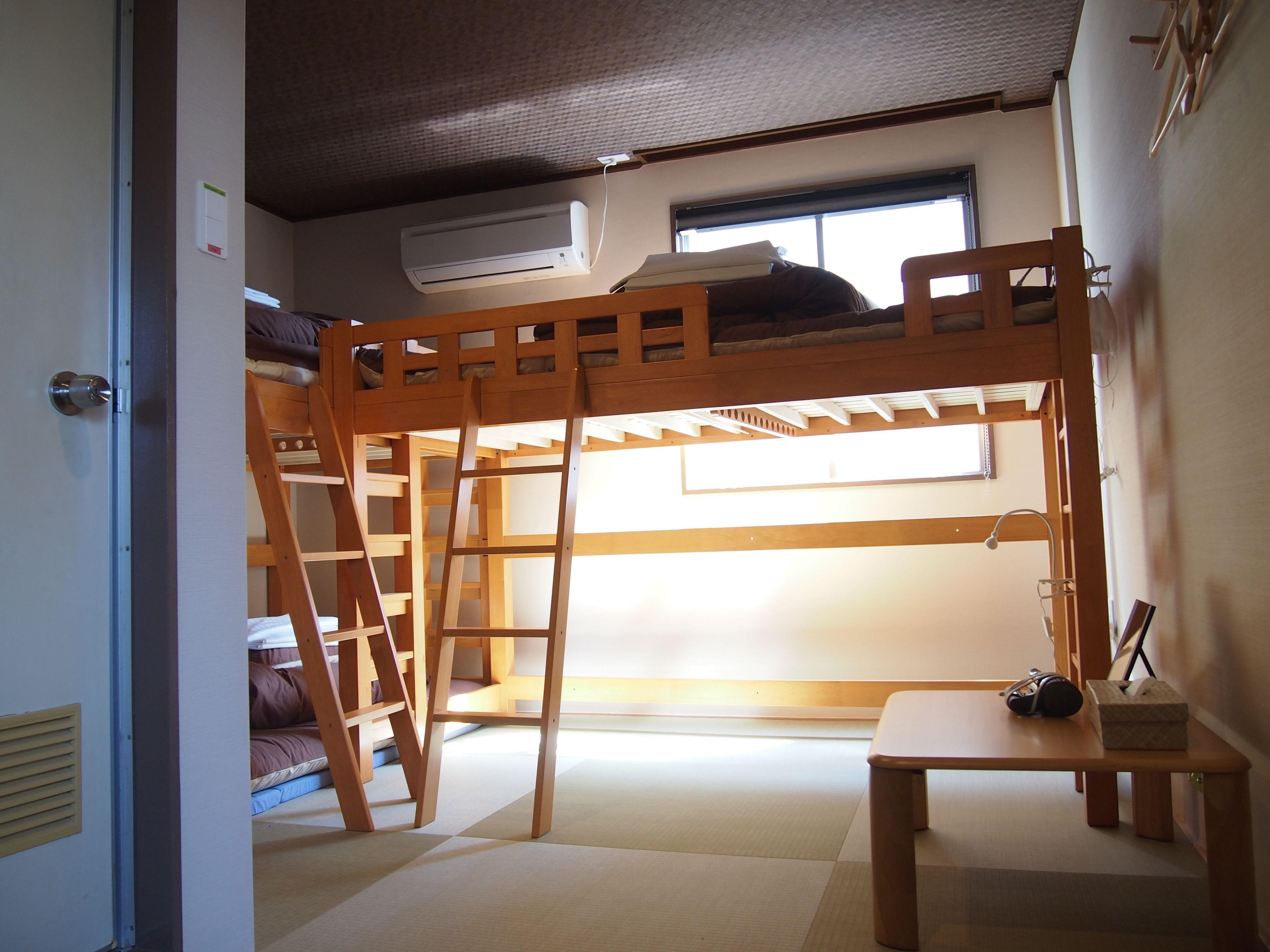 A bunk bed room with a ladder, a desk, a chair, and a window.