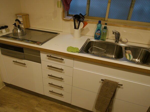 A kitchen with a dishwasher, a kettle, a sink, and various kitchen utensils.