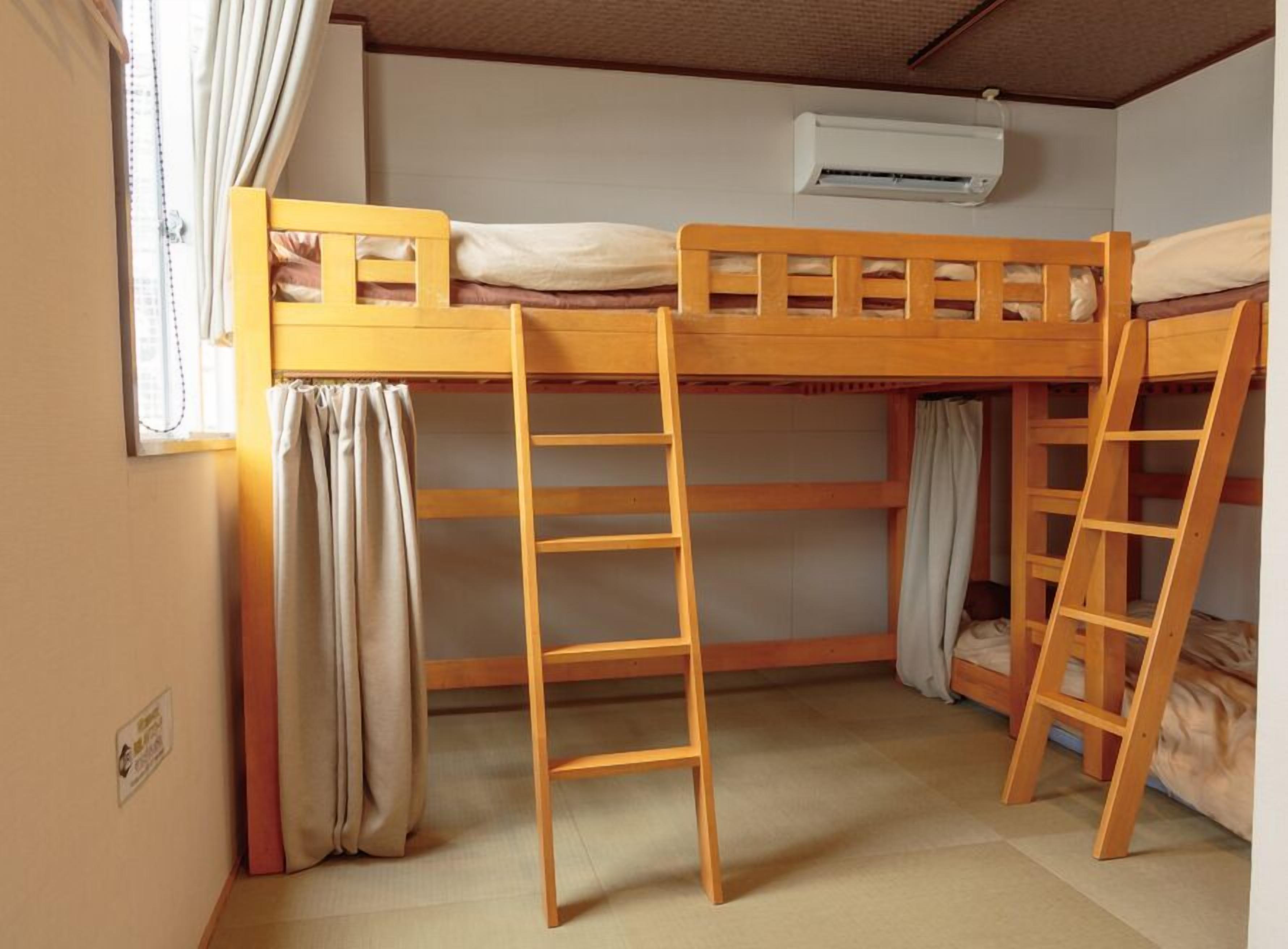 Ein Schlafzimmer mit Etagenbetten, einer Leiter, einem Fenster mit Vorhängen und einer Klimaanlage.