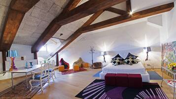 A spacious loft bedroom with exposed wooden beams, a large bed, a desk, and a dining area.