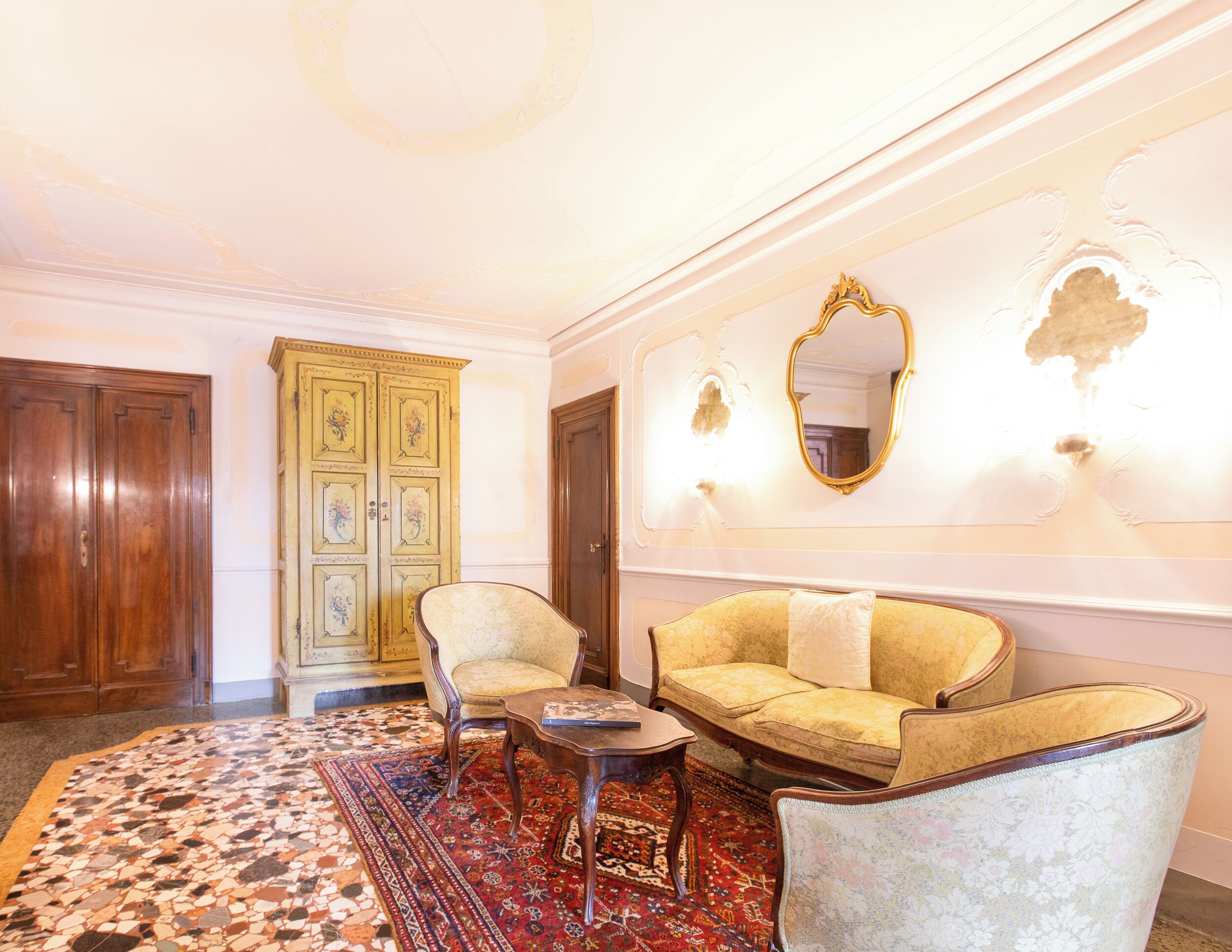 Une pièce avec un sol à motifs, un canapé, deux fauteuils, une petite table et une armoire en bois.